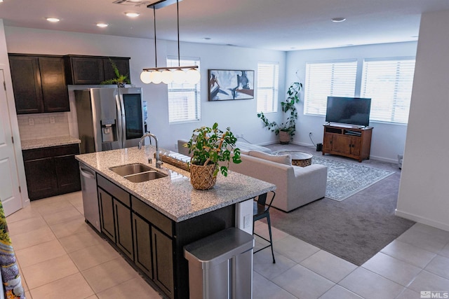 kitchen featuring sink, light tile patterned floors, stainless steel appliances, and a kitchen island with sink