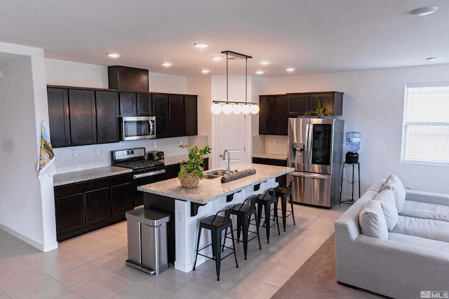 kitchen featuring decorative backsplash, appliances with stainless steel finishes, sink, decorative light fixtures, and an island with sink