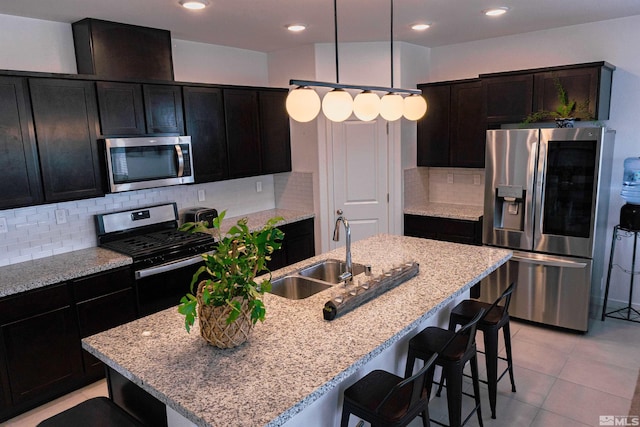 kitchen with decorative backsplash, appliances with stainless steel finishes, a kitchen island with sink, sink, and pendant lighting