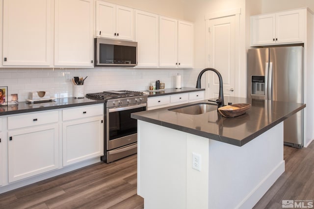 kitchen with appliances with stainless steel finishes, white cabinetry, a kitchen island with sink, and sink