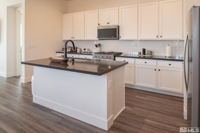 kitchen with dark hardwood / wood-style flooring, stainless steel appliances, sink, white cabinetry, and an island with sink