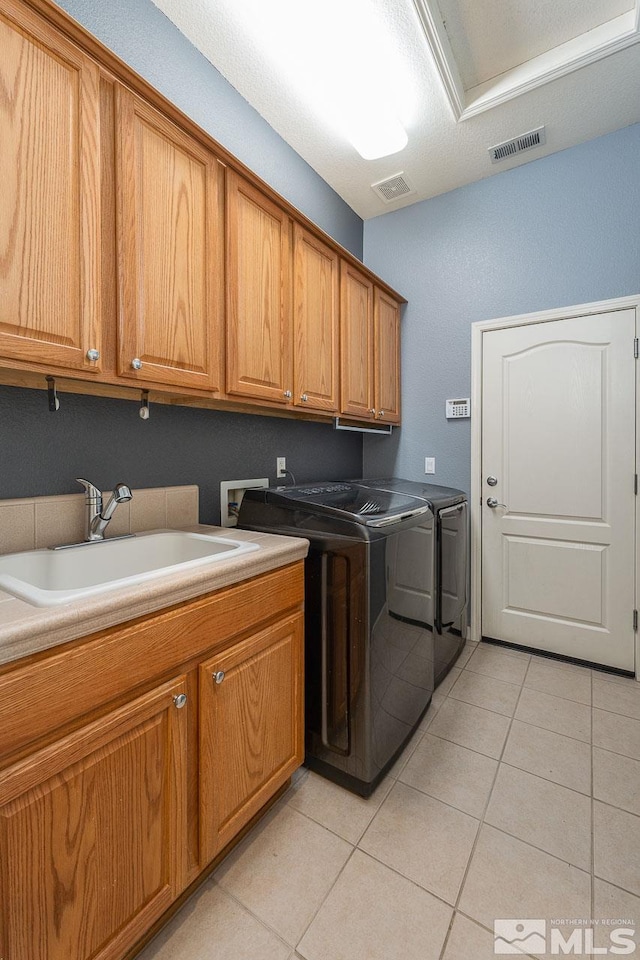 clothes washing area featuring separate washer and dryer, sink, light tile patterned floors, and cabinets