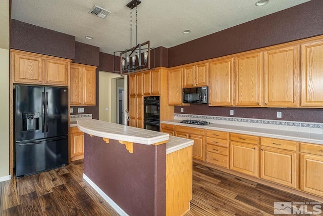 kitchen with a center island, hanging light fixtures, dark wood-type flooring, tile countertops, and black appliances