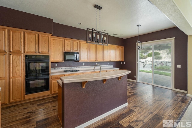 kitchen featuring dark hardwood / wood-style flooring, tile countertops, pendant lighting, a center island with sink, and black appliances