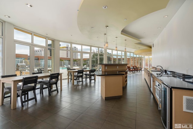 kitchen featuring pendant lighting, a kitchen island, wine cooler, a tray ceiling, and expansive windows