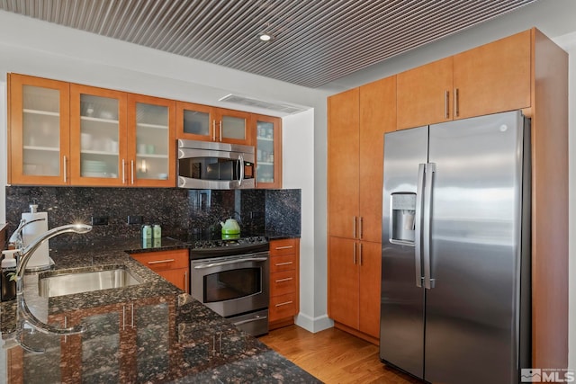 kitchen featuring light hardwood / wood-style flooring, sink, dark stone countertops, decorative backsplash, and stainless steel appliances