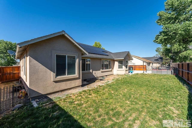 rear view of property featuring a yard and solar panels