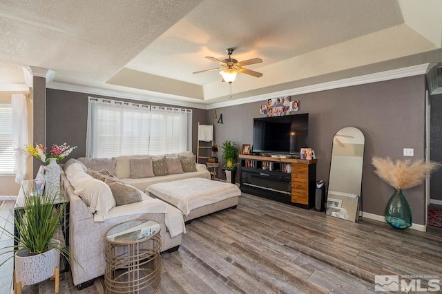 living room with ceiling fan, crown molding, wood-type flooring, a textured ceiling, and a tray ceiling