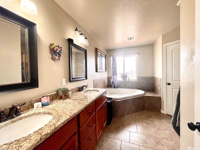 bathroom featuring dual sinks, tile flooring, vanity with extensive cabinet space, tiled tub, and a textured ceiling