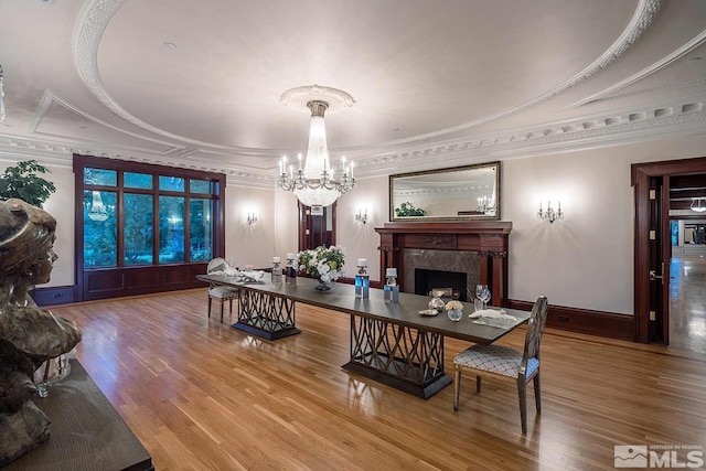 interior space featuring a tray ceiling, wood-type flooring, a notable chandelier, crown molding, and a high end fireplace