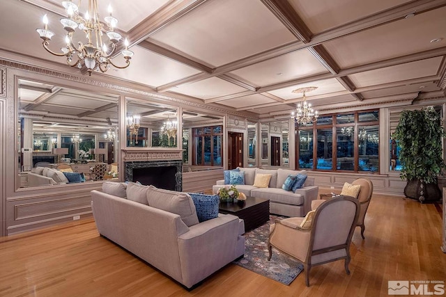living room with coffered ceiling, a fireplace, light wood-style floors, and an inviting chandelier