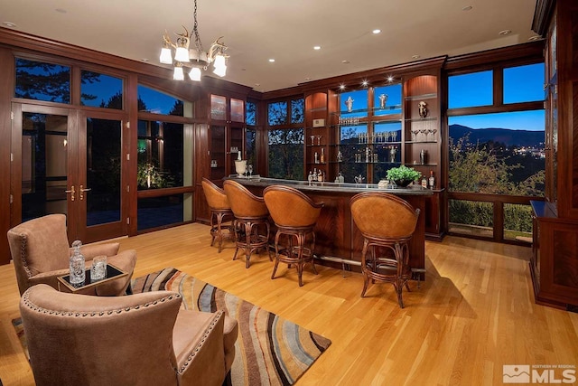 bar with light hardwood / wood-style flooring, a mountain view, a chandelier, decorative light fixtures, and a wall of windows