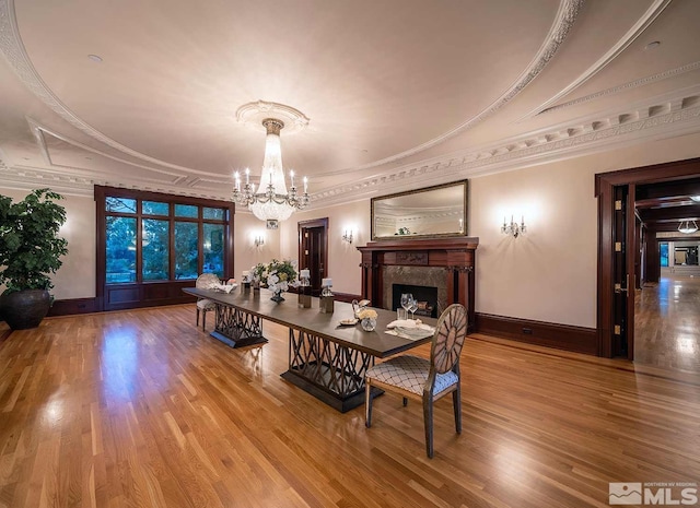 dining area featuring a notable chandelier, wood finished floors, ornamental molding, and a premium fireplace