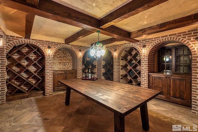 wine area with beamed ceiling, stone tile flooring, and brick wall