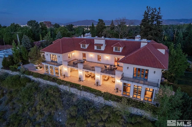 back of house featuring a tile roof, a balcony, and stucco siding