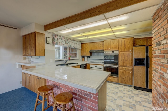 kitchen with sink, tile countertops, kitchen peninsula, exhaust hood, and black appliances