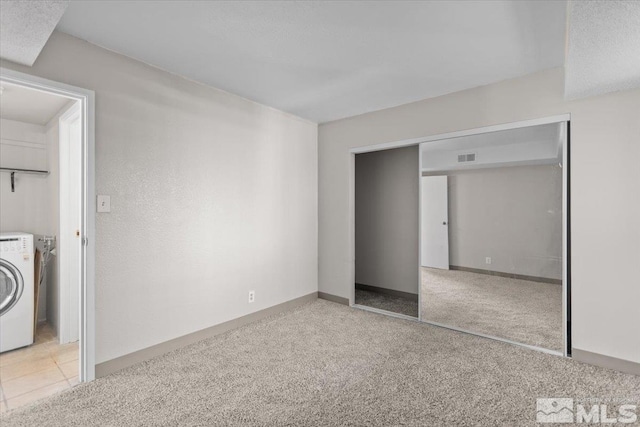 unfurnished bedroom with washer / dryer, light colored carpet, and a closet