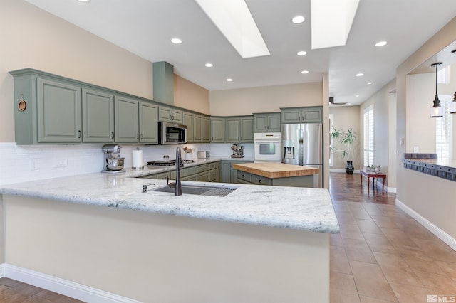 kitchen with kitchen peninsula, appliances with stainless steel finishes, backsplash, a skylight, and butcher block counters