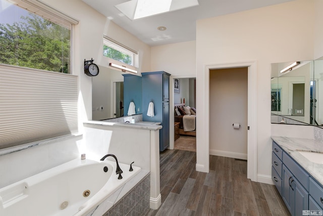 bathroom with wood-type flooring, vanity, a skylight, and a relaxing tiled tub