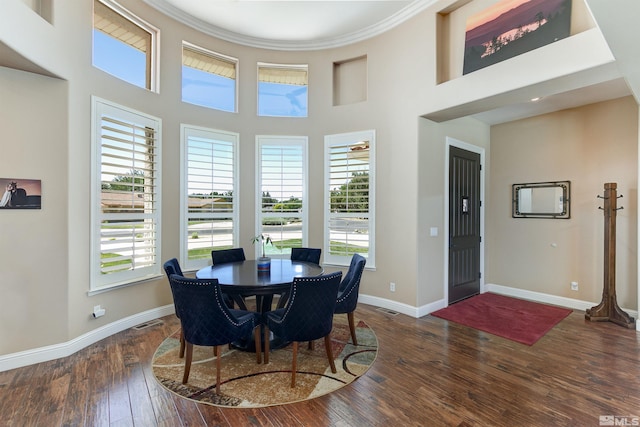 dining area with dark hardwood / wood-style floors, ornamental molding, and a towering ceiling