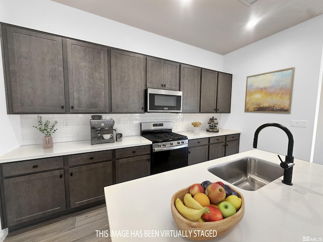 kitchen with sink, backsplash, light hardwood / wood-style floors, dark brown cabinets, and appliances with stainless steel finishes