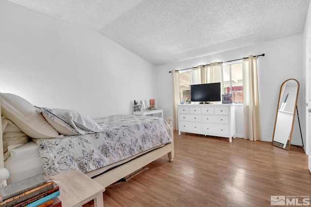 bedroom with lofted ceiling, a textured ceiling, and light hardwood / wood-style flooring