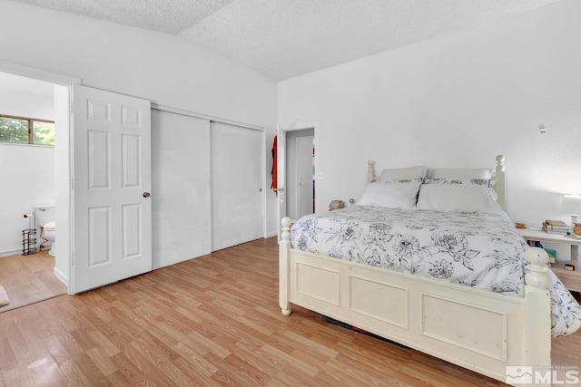 bedroom featuring a textured ceiling, light wood-type flooring, a closet, and lofted ceiling