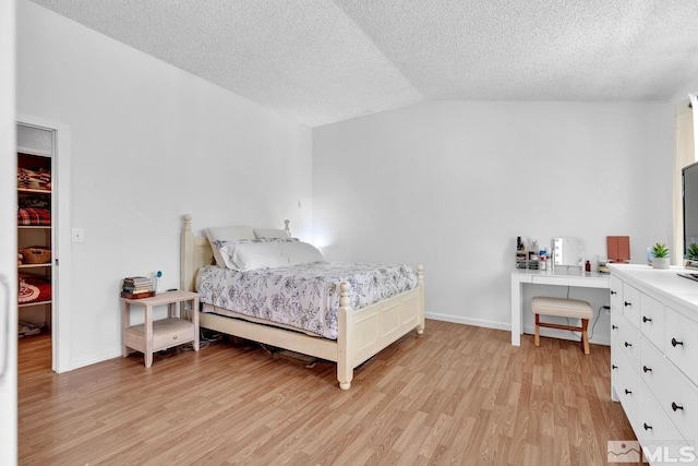 bedroom featuring a textured ceiling, light hardwood / wood-style flooring, and vaulted ceiling