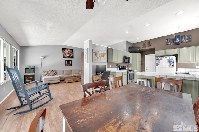 dining space featuring ceiling fan, light hardwood / wood-style floors, a textured ceiling, and vaulted ceiling