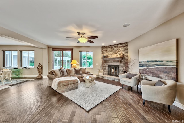 living room featuring ceiling fan, a stone fireplace, and dark hardwood / wood-style flooring