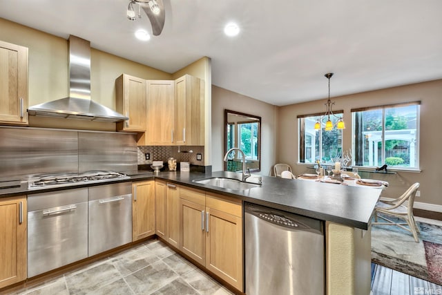 kitchen with kitchen peninsula, wall chimney exhaust hood, stainless steel appliances, sink, and plenty of natural light