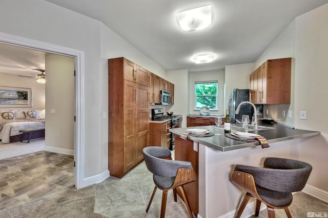 kitchen with sink, ceiling fan, appliances with stainless steel finishes, kitchen peninsula, and a breakfast bar area