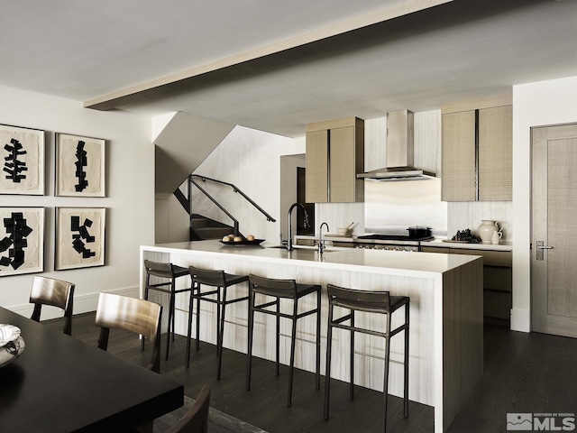 kitchen with a breakfast bar area, dark hardwood / wood-style flooring, wall chimney range hood, a kitchen island with sink, and backsplash