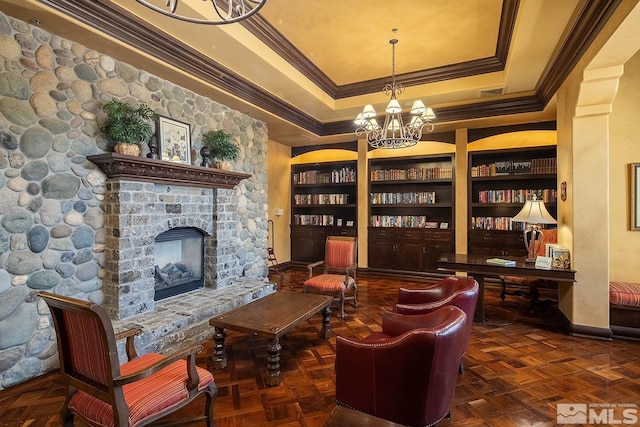 living area with dark parquet flooring, a stone fireplace, built in features, and a notable chandelier