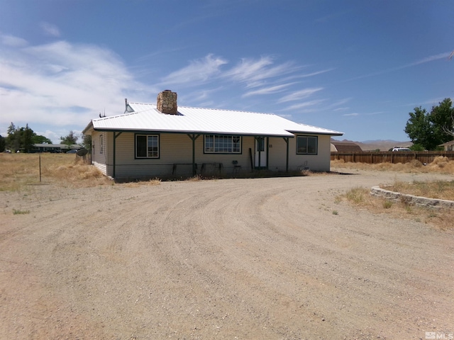 view of front of property with metal roof, driveway, a chimney, and fence