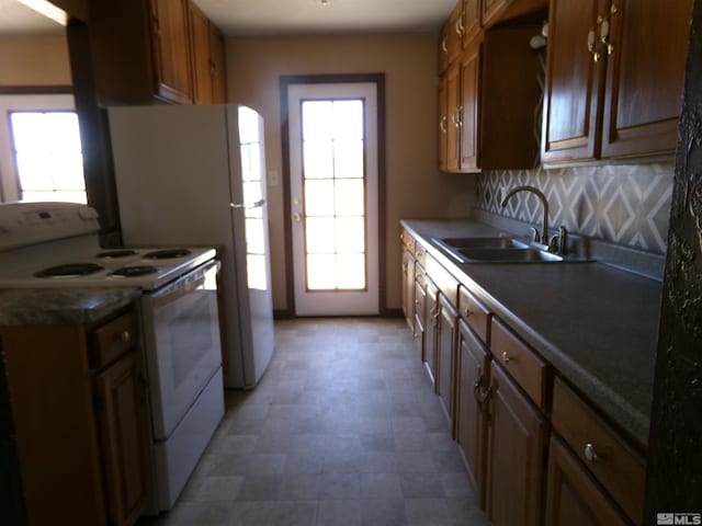 kitchen with brown cabinets, dark countertops, white electric range, a healthy amount of sunlight, and a sink