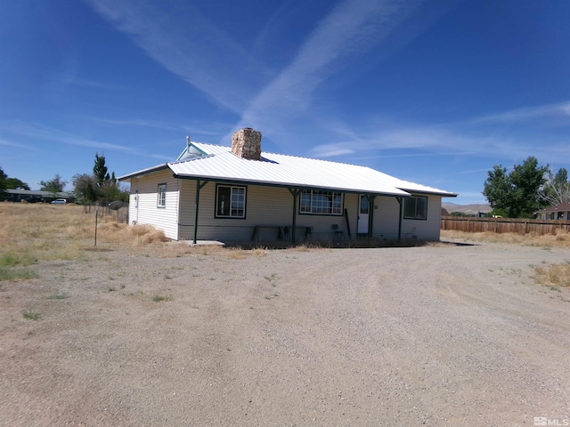 view of front of home with driveway, metal roof, a chimney, and fence