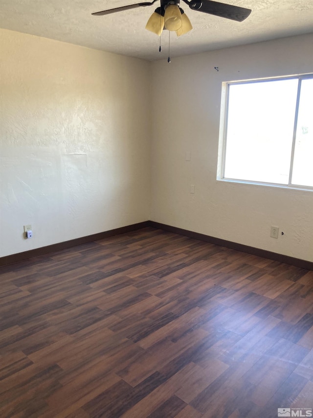 spare room with a textured ceiling, dark wood-style flooring, and baseboards