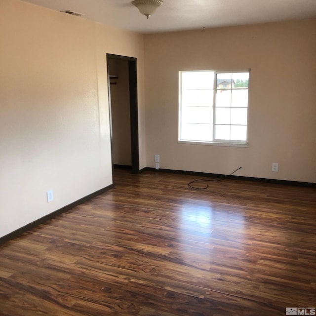 spare room with dark wood-style floors, baseboards, and visible vents