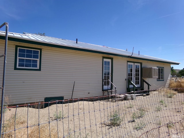 rear view of house with entry steps, metal roof, and fence