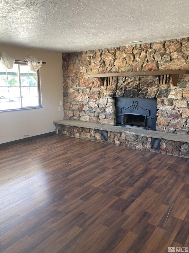 unfurnished living room featuring visible vents, dark wood finished floors, a textured ceiling, and a stone fireplace