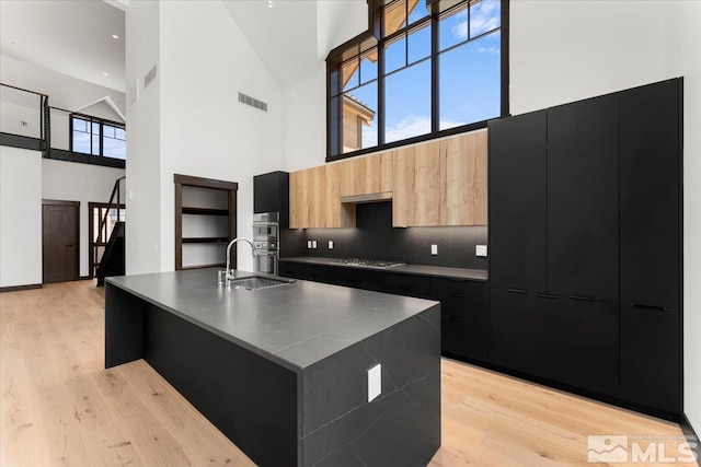 kitchen featuring light wood-type flooring, a center island with sink, and high vaulted ceiling