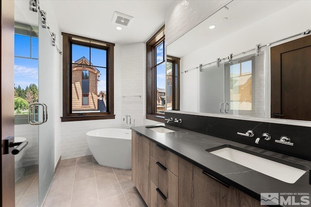 bathroom featuring a bath, vanity, tile patterned floors, and tile walls