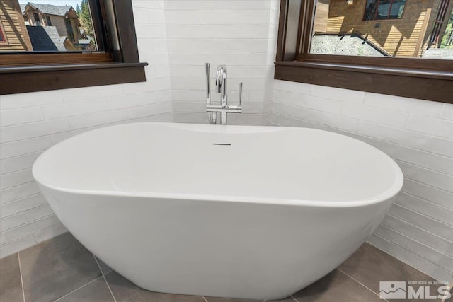 bathroom with tile patterned flooring, tile walls, and a tub