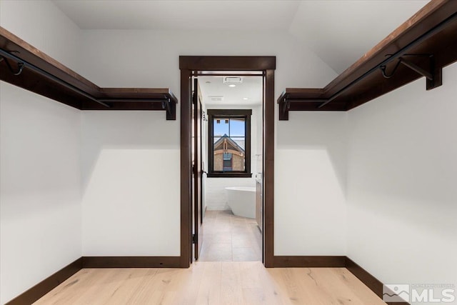 spacious closet with light hardwood / wood-style floors and lofted ceiling