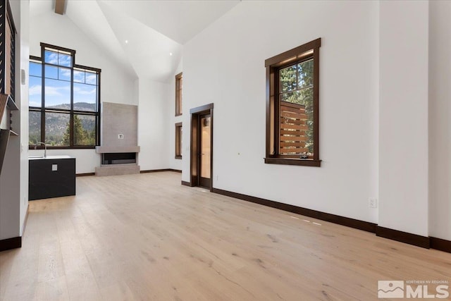 unfurnished living room featuring light hardwood / wood-style floors, beam ceiling, and high vaulted ceiling