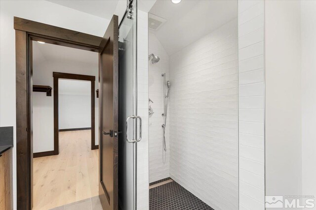 bathroom with hardwood / wood-style floors, a shower with shower door, and vaulted ceiling