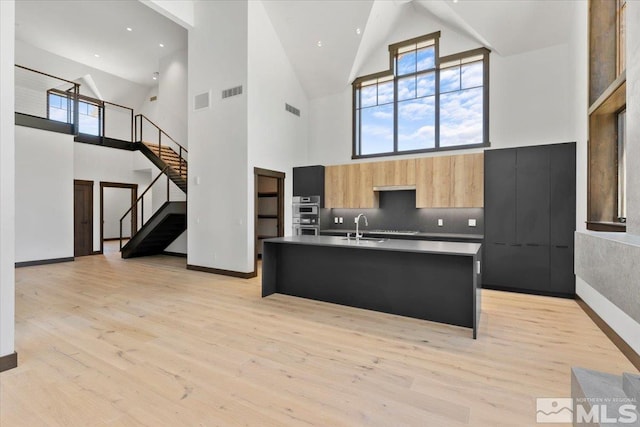 kitchen featuring high vaulted ceiling, a center island with sink, sink, light wood-type flooring, and a kitchen bar