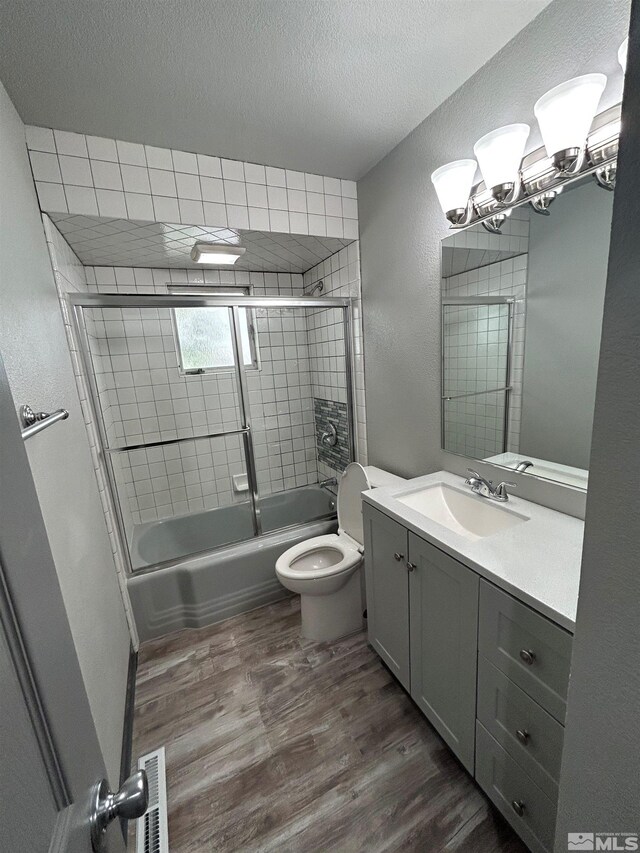 full bathroom featuring enclosed tub / shower combo, oversized vanity, toilet, hardwood / wood-style flooring, and a textured ceiling