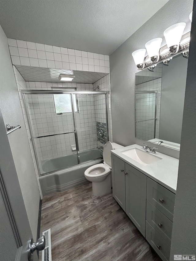 full bathroom with combined bath / shower with glass door, hardwood / wood-style floors, vanity, a textured ceiling, and toilet